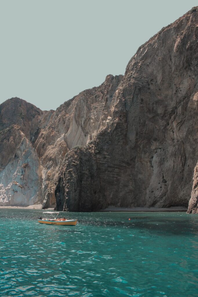 the island of Ponza; a small yellow boat floating in front of sharp cliffs going straight into clear blue green water
