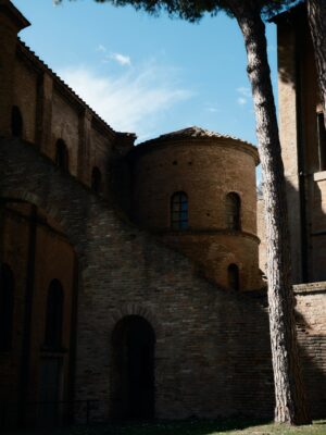 a shaded stone tower in Ravenna with a single tall tree out front