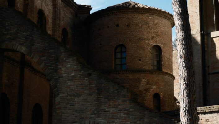 a shaded stone tower in Ravenna with a single tall tree out front