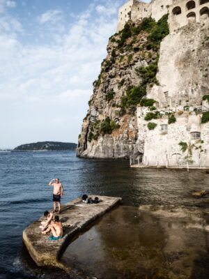 people standing on a concrete jut out into still water near a rocky cliff on the sea