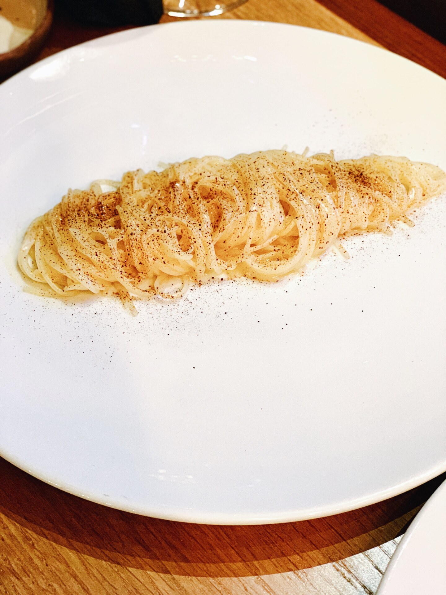 a white plate with a a twirl of light colored spaghetti perfectly down the middle covered in black pepper