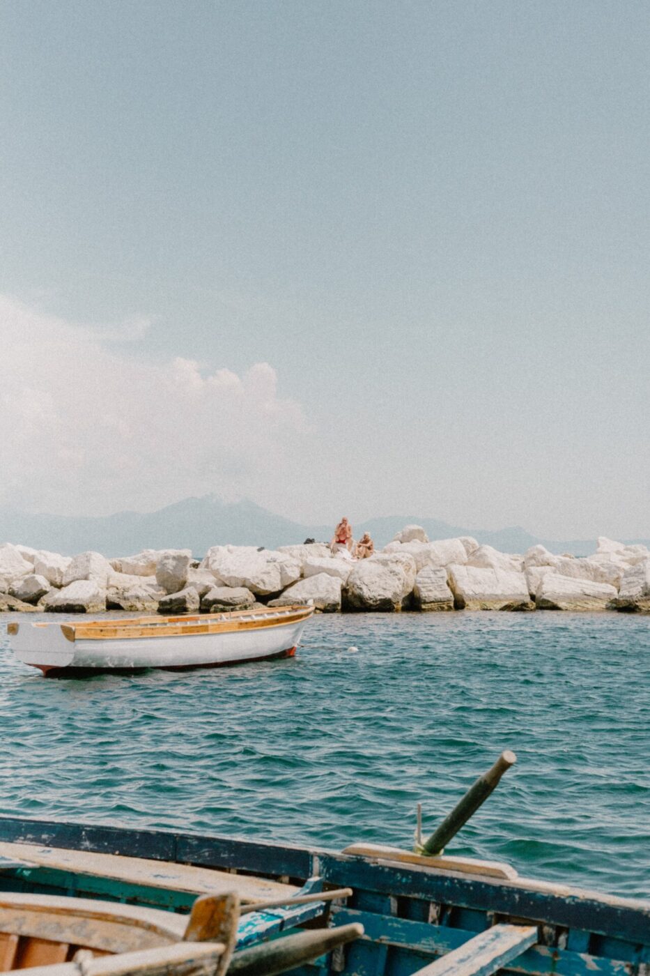 an image by Gina Spinelli of a small wooden boat in a light blue cove near some white rocks