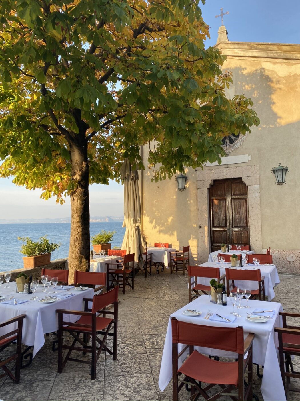 the terrace at Punta San Vigilio overlooking the lake with trees nearby with tables set nicely with red table cloths