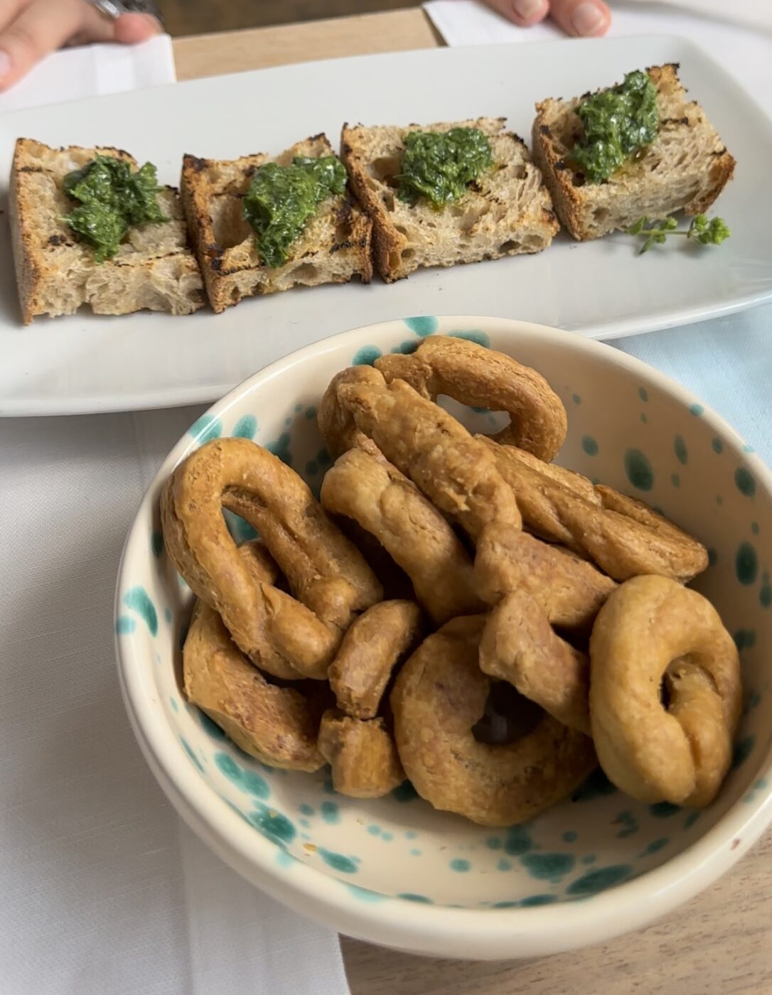 a bowl of taralli in a ceramic bowl with blue spots and a platter of four bruschetta with pesto