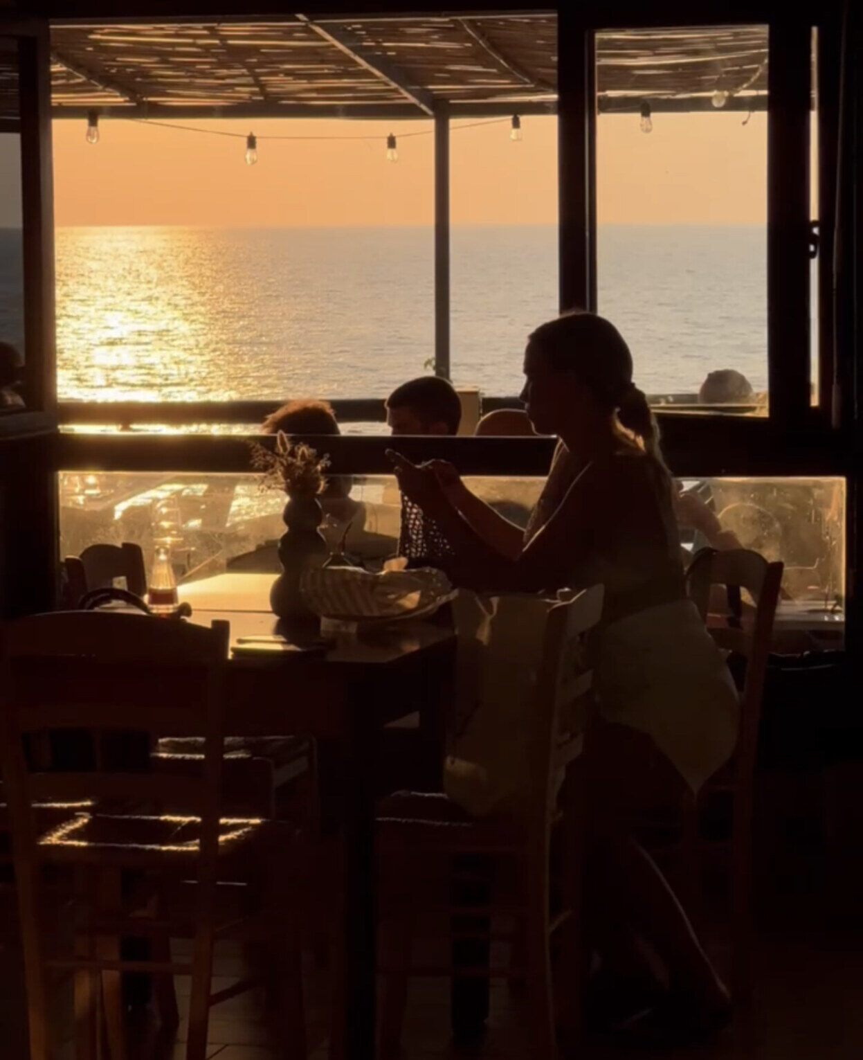 sunset through the window of a restaurant with the outline of a woman sitting at a table on Giglio