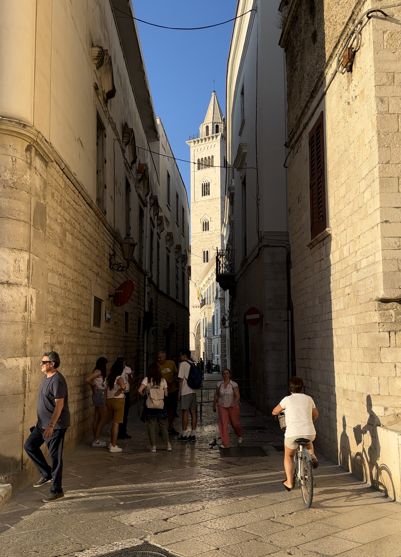 a narrow street in Puglia opening up to a church in the distance with bright blue sky