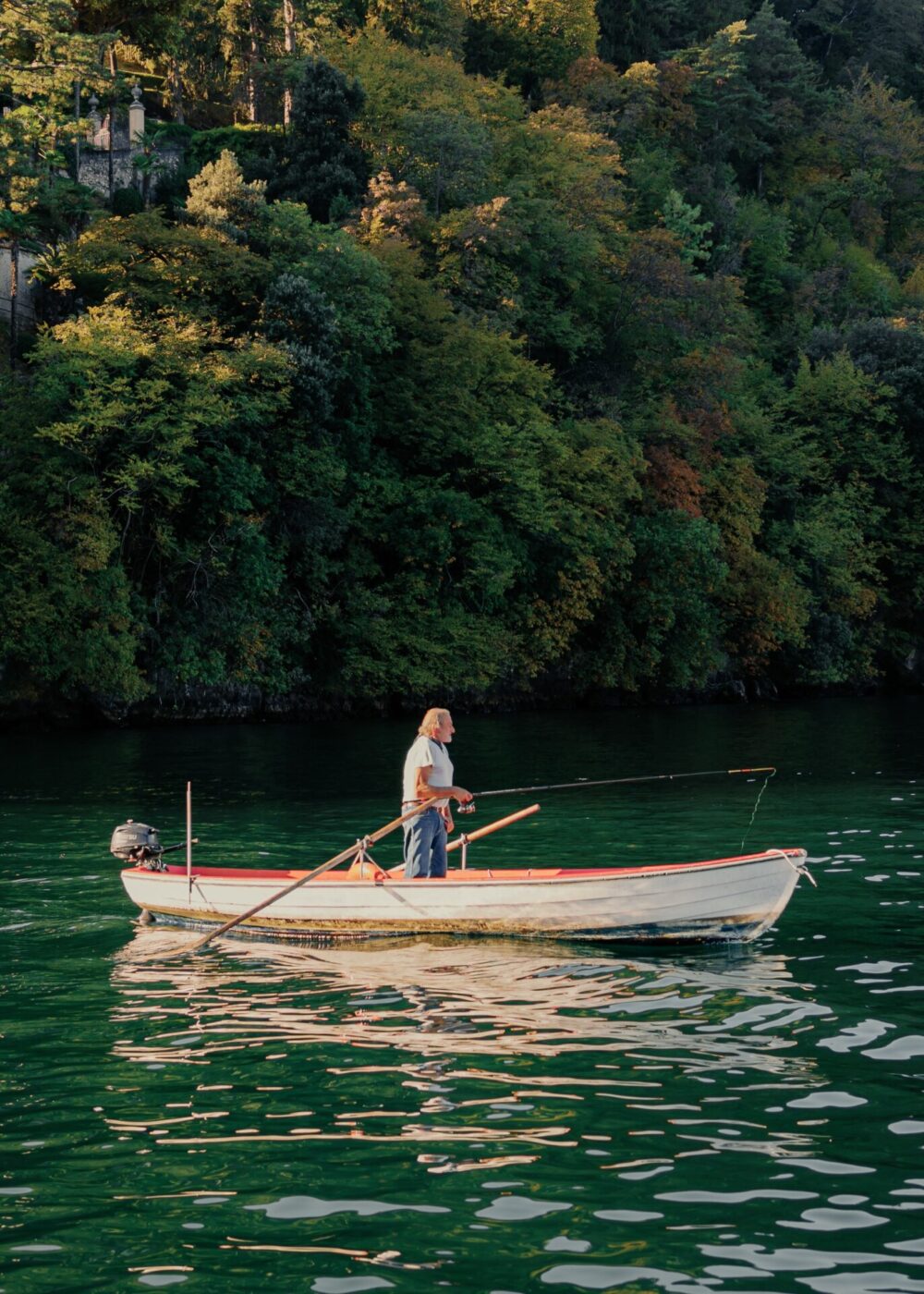 a man in a small boat standing and fishing in a clear lake