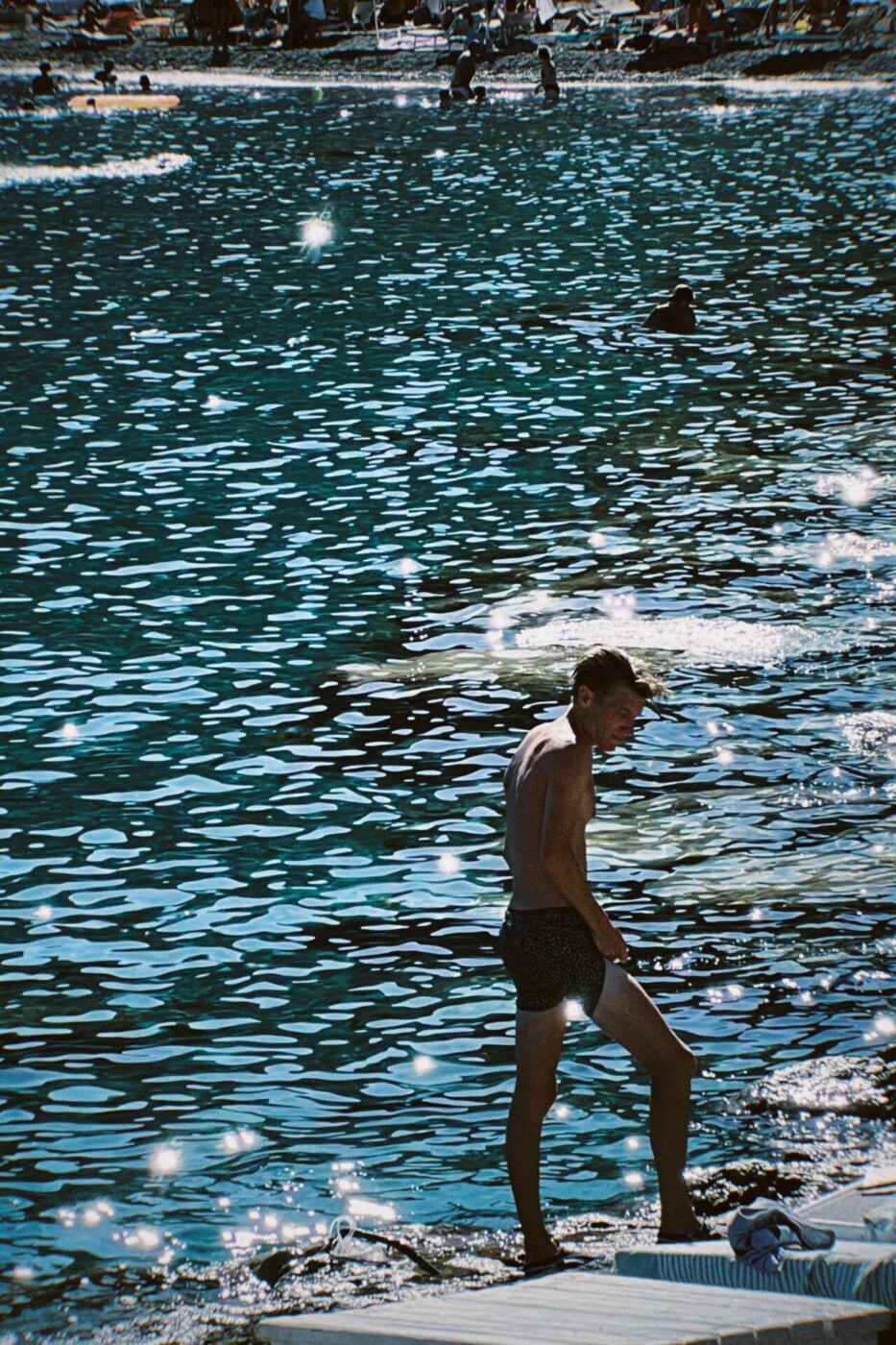 a man standing on a rock next to the sea that is bright blue and extremely sparkly