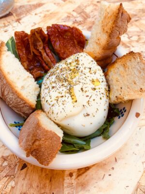 a bowl of salad topped with a large burrata and slices of bread