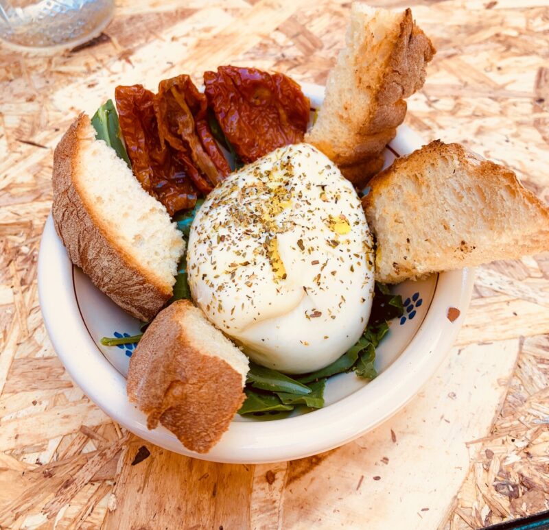 a bowl of salad topped with a large burrata and slices of bread