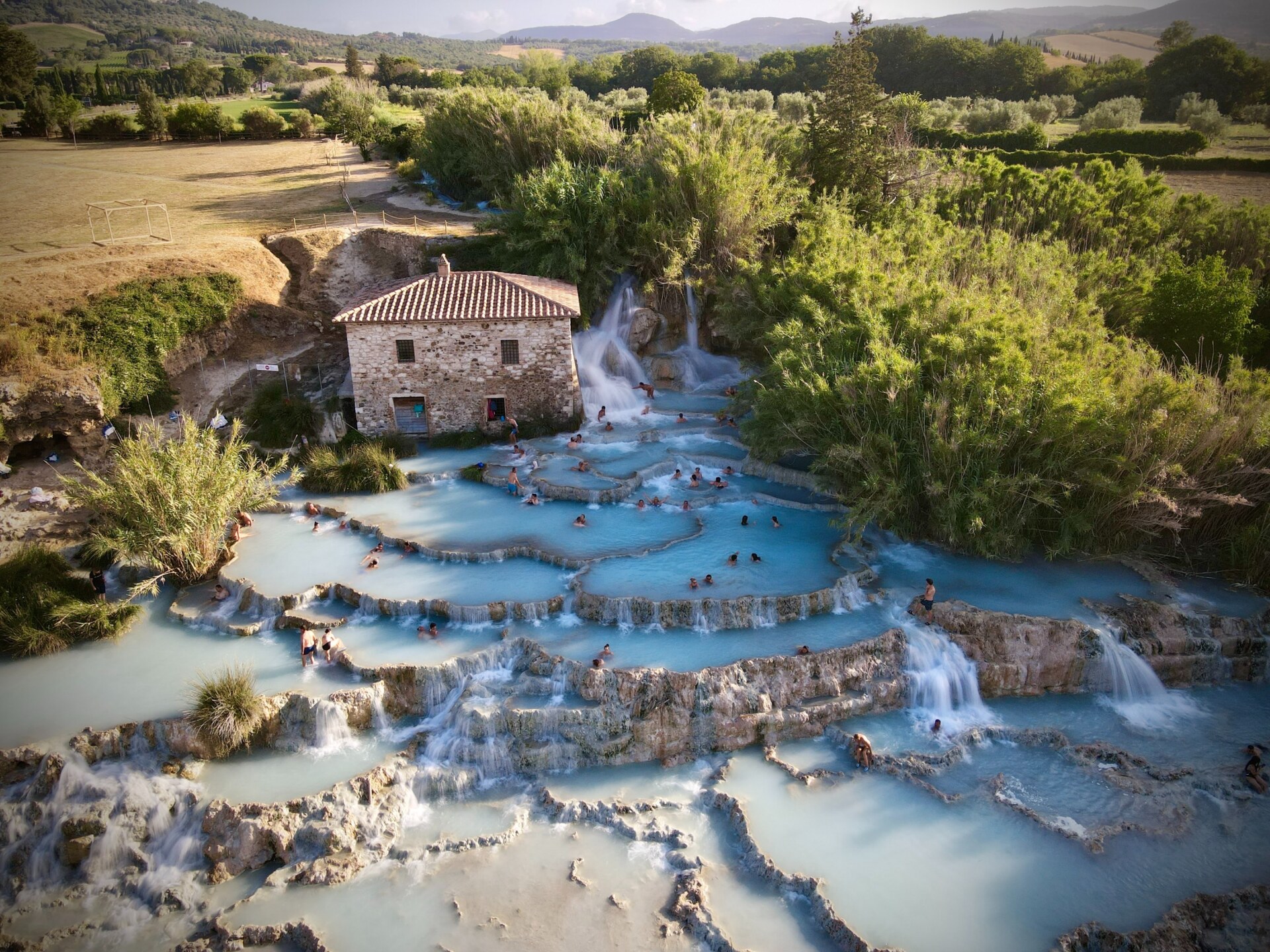 the waterfalling hot springs at Saturnia with a rustic house and pale green trees all around