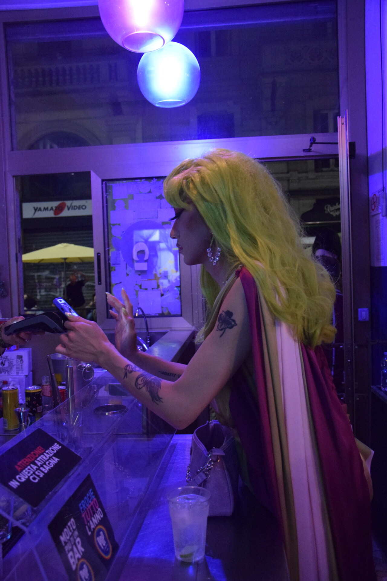 a drag queen with green hair ordering a drink at a bar