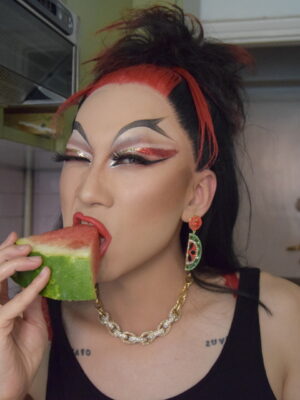 a drag queen with dramatic black and red makeup eating a piece of watermelon