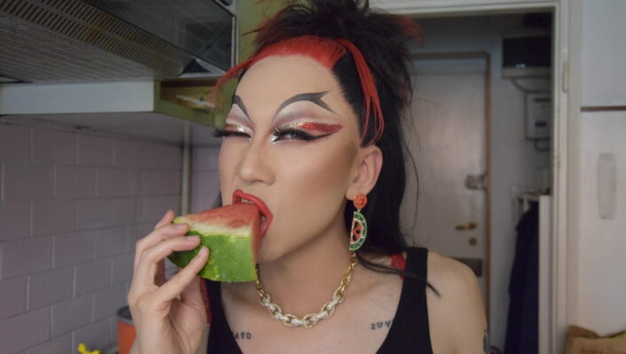 a drag queen with dramatic black and red makeup eating a piece of watermelon