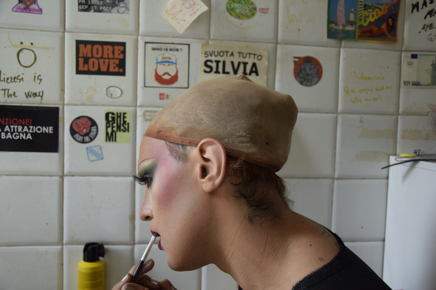 a drag queen doing their makeup getting ready for show and wearing a wig cap