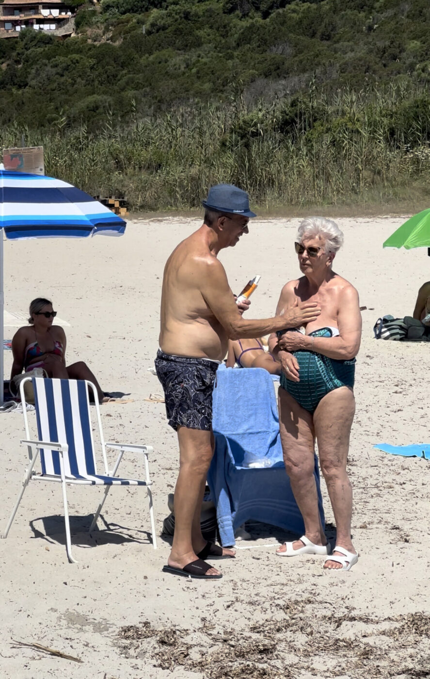 an older couple at the beach putting sunscreen on each other