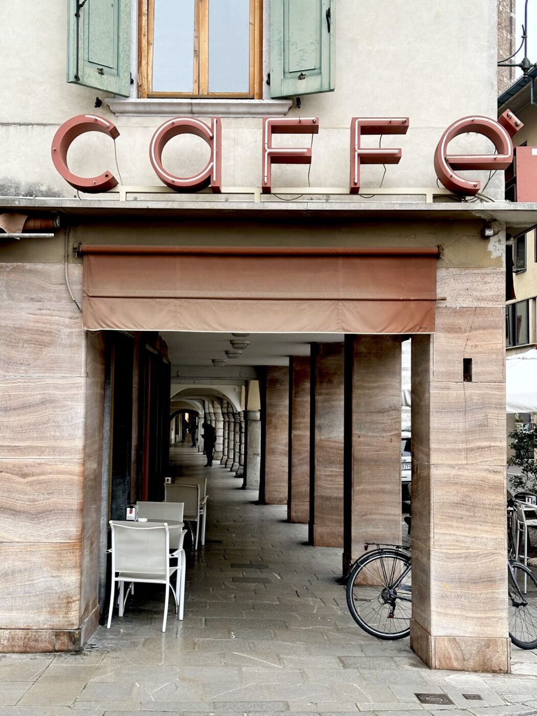 a lowercase red neon sign for a caffe taken during the day looking down the porticos