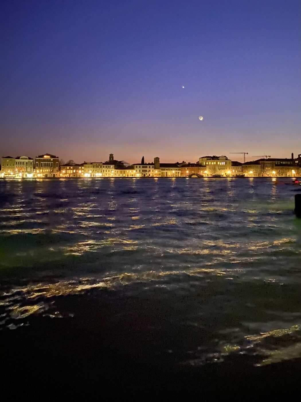 a photo from the water looking back at the light up coast and the sunset over the town