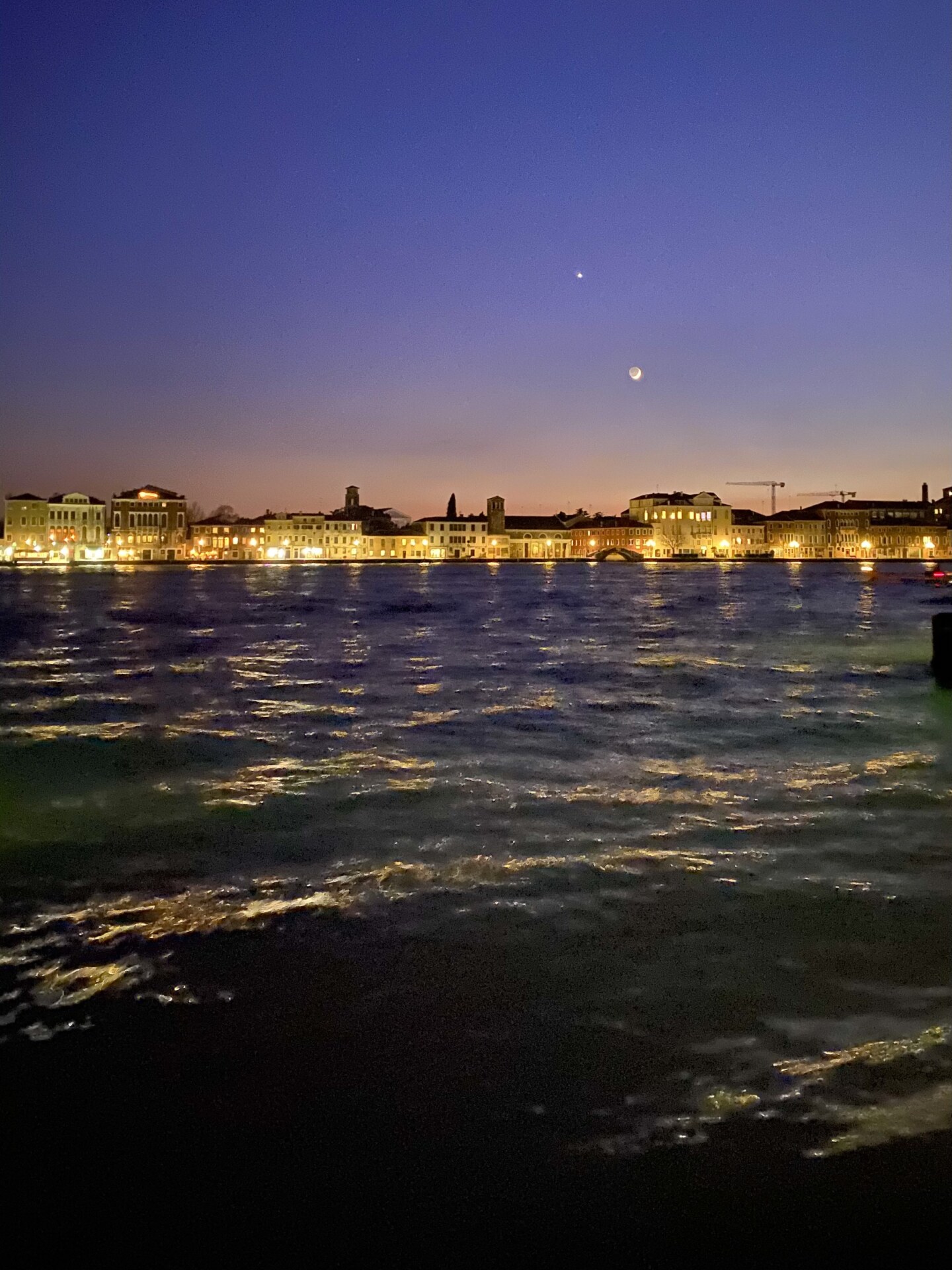 a photo from the water looking back at the light up coast and the sunset over the town