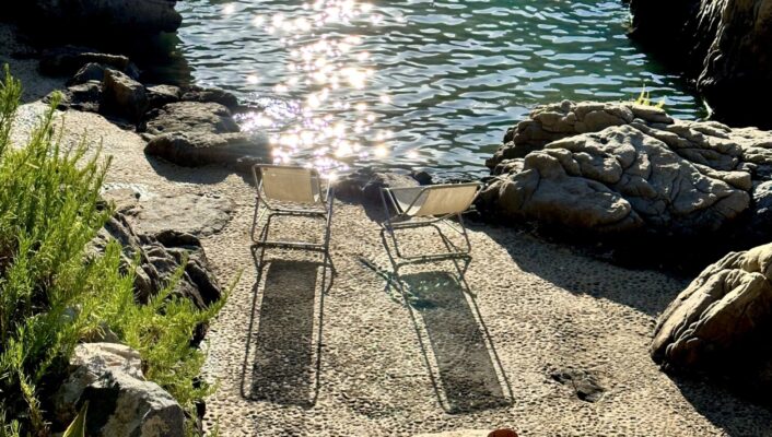 two chairs sitting in a tiny cove at Le Calette against the crystal clear sparkling water