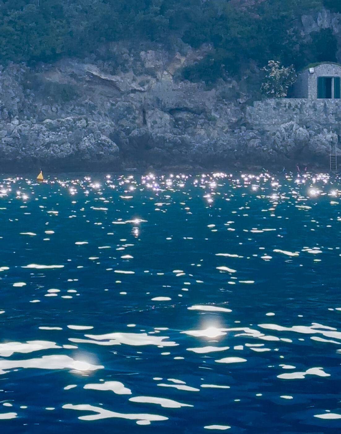 an image of the bright blue shimmering sea along the rocky shore in Naples