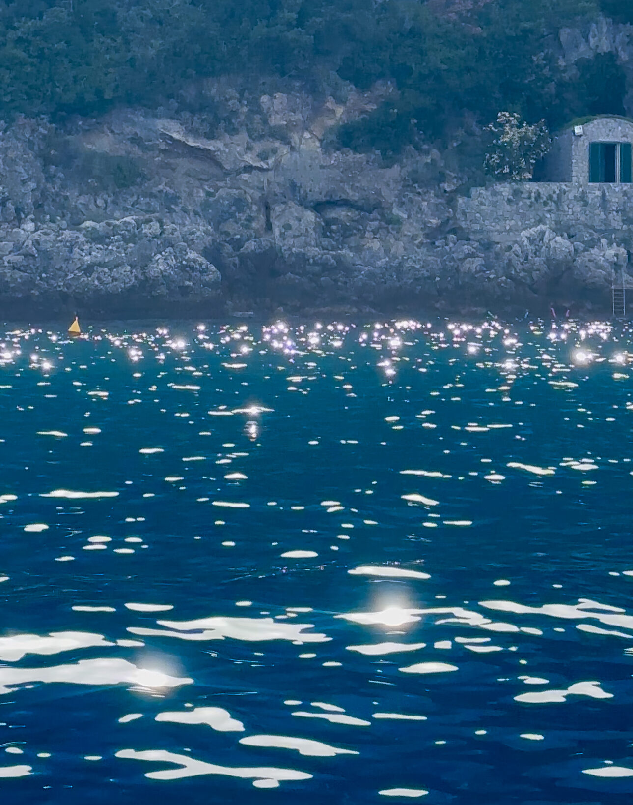 an image of the bright blue shimmering sea along the rocky shore in Naples