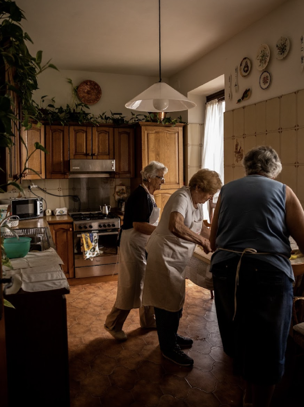 a photo by Letizia Cigliutti of three nonne making plin in their kitchen, photographed from the back bending over a table