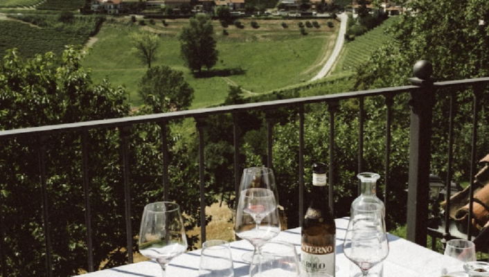 photo by Letizia Cigliutti of a table on a terrace overlooking the rolling hills of monforte d'alba with a bottle of barolo, empty wine glasses, and empty espresso cups
