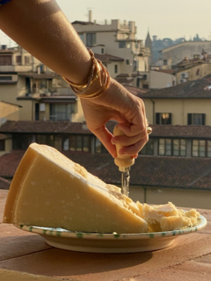 a large chunk of parmesan sitting on a plate on a balcony in florence and someone is cutting a chunk