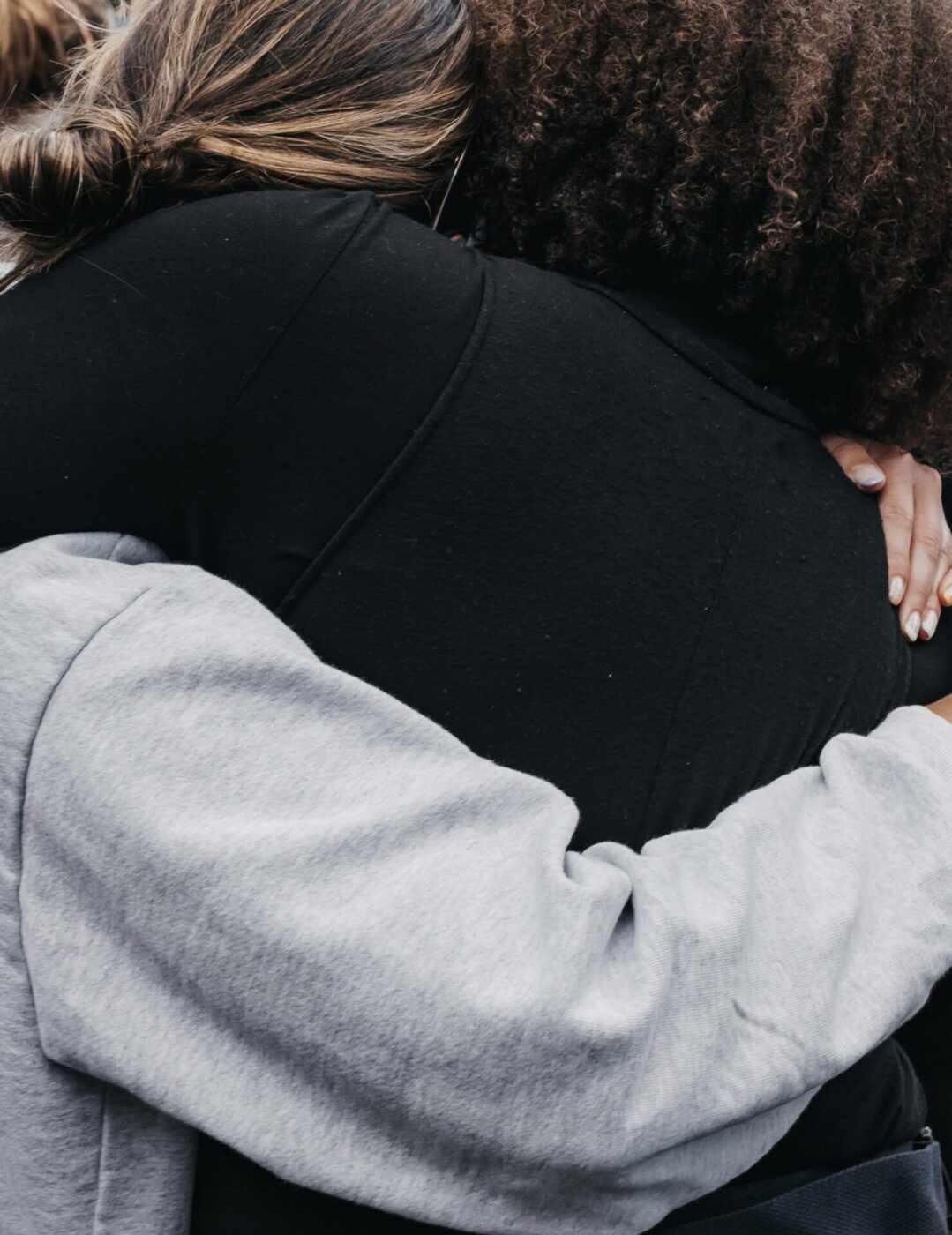 two girls hugging one wearing a grey sweater and one black