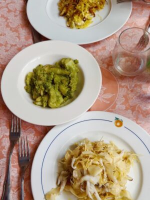 three white plates filled with Broccolo romano ripassato and cuttlefish with artichokes on a pink tablecloth