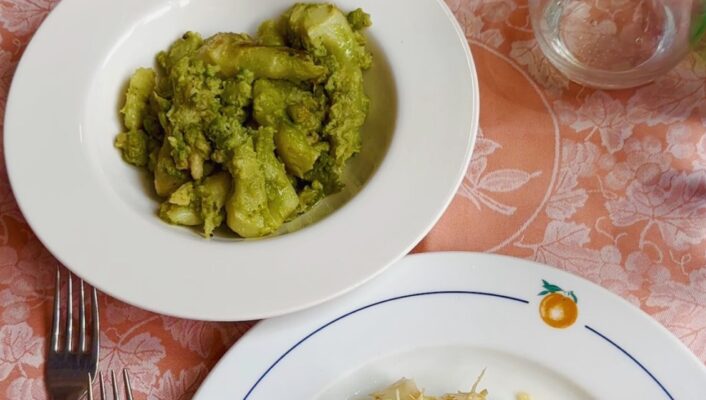 three white plates filled with Broccolo romano ripassato and cuttlefish with artichokes on a pink tablecloth