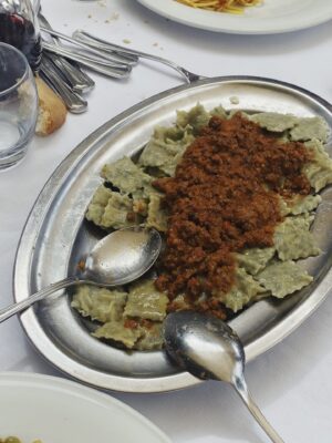 a silver platter of little green ravioli covered in meat sauce