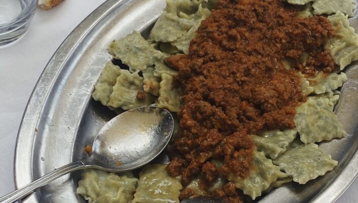 a silver platter of little green ravioli covered in meat sauce