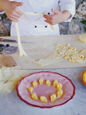 a person in a chef's coat making homemade tagliatelle and a plate of tortellini in the front