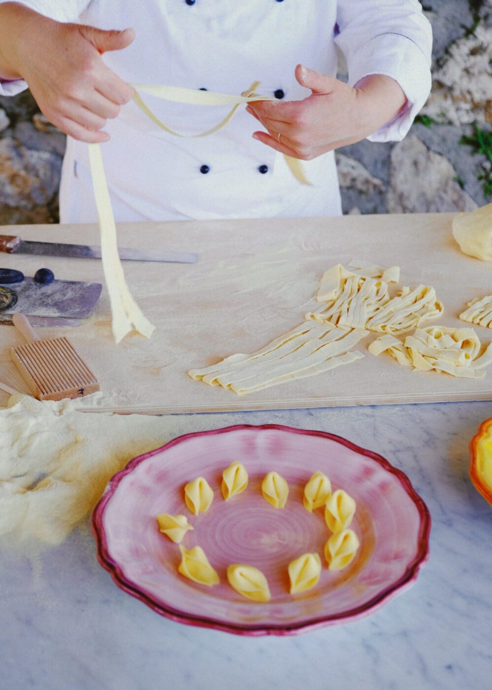 a person in a chef's coat making homemade tagliatelle and a plate of tortellini in the front