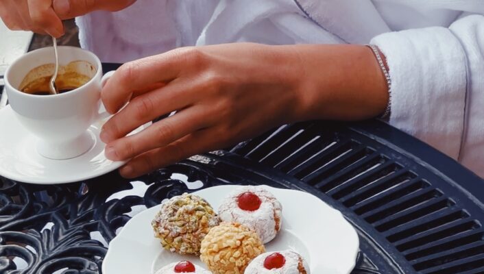 a man stirring a small espresso cup with a plate of small pastries next to him