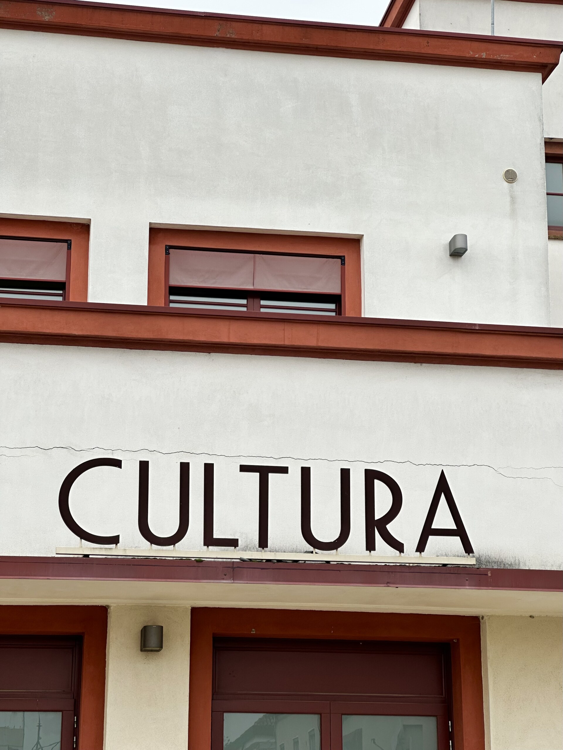 Image Title - Facade of a building with the word CULTURA in large letters. The building is cream-colored with red trim, featuring rectangular windows above the entrance.