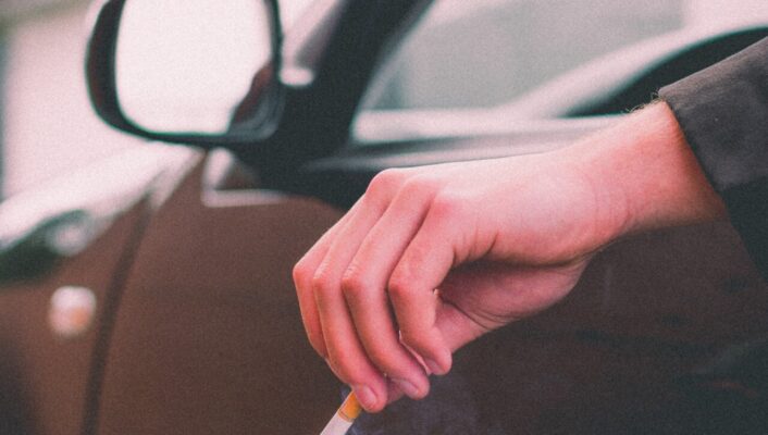 An image of a black car with a man holding a cigarette out the open window