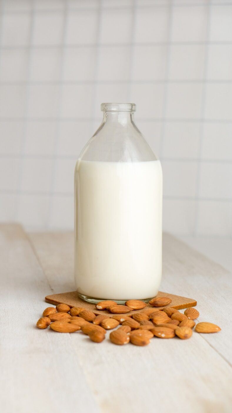 a glass carafe of almond milk next to a pile of raw almonds