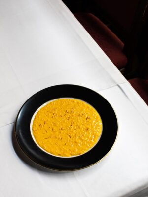 an image of bright yellow risotto alla milanese on a black plate from Da Giacomo