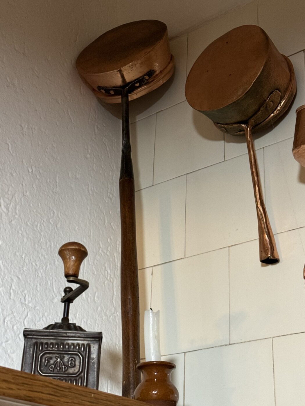 two copper Scaldini hanging against a white tile wall from a market in Puglia