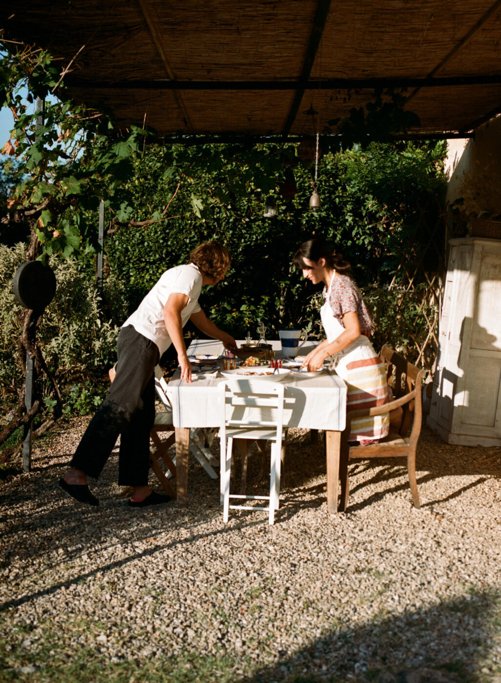 an image of two women setting a table outside under trees at a Tuscan farmhouse