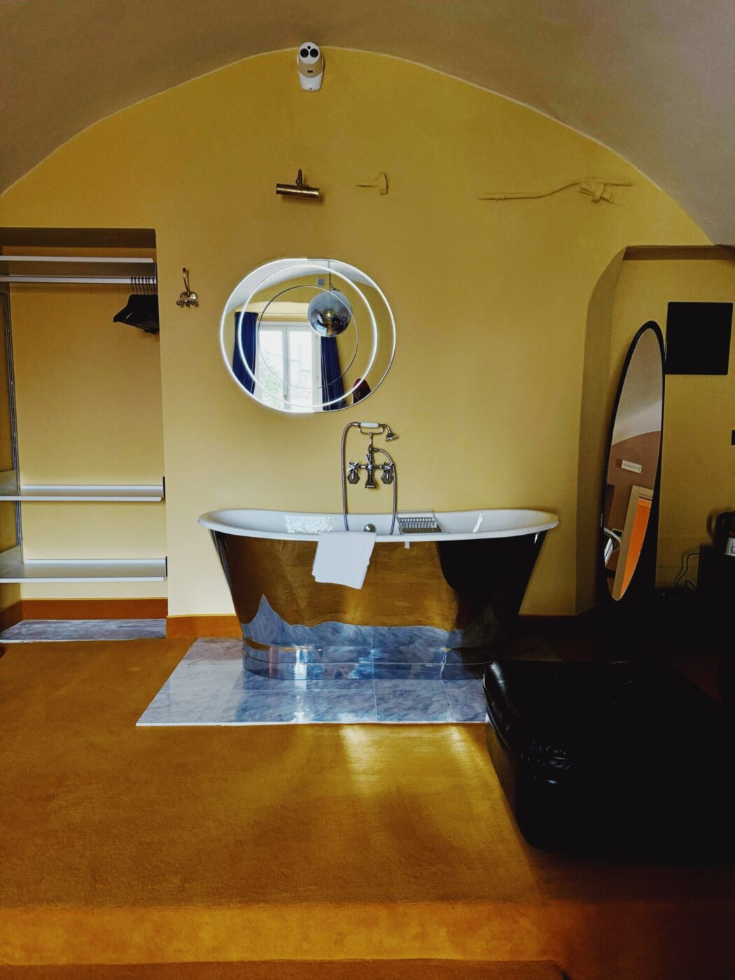 a huge brass tub in a dark yellow colored bathroom with a large circular mirror at stella d'italia