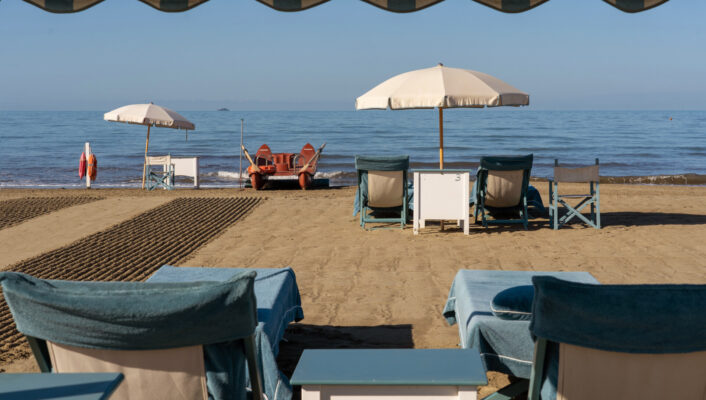 an image of blue lounge chairs and white beach umbrellas on the sandy beach near Locanda Al Colle