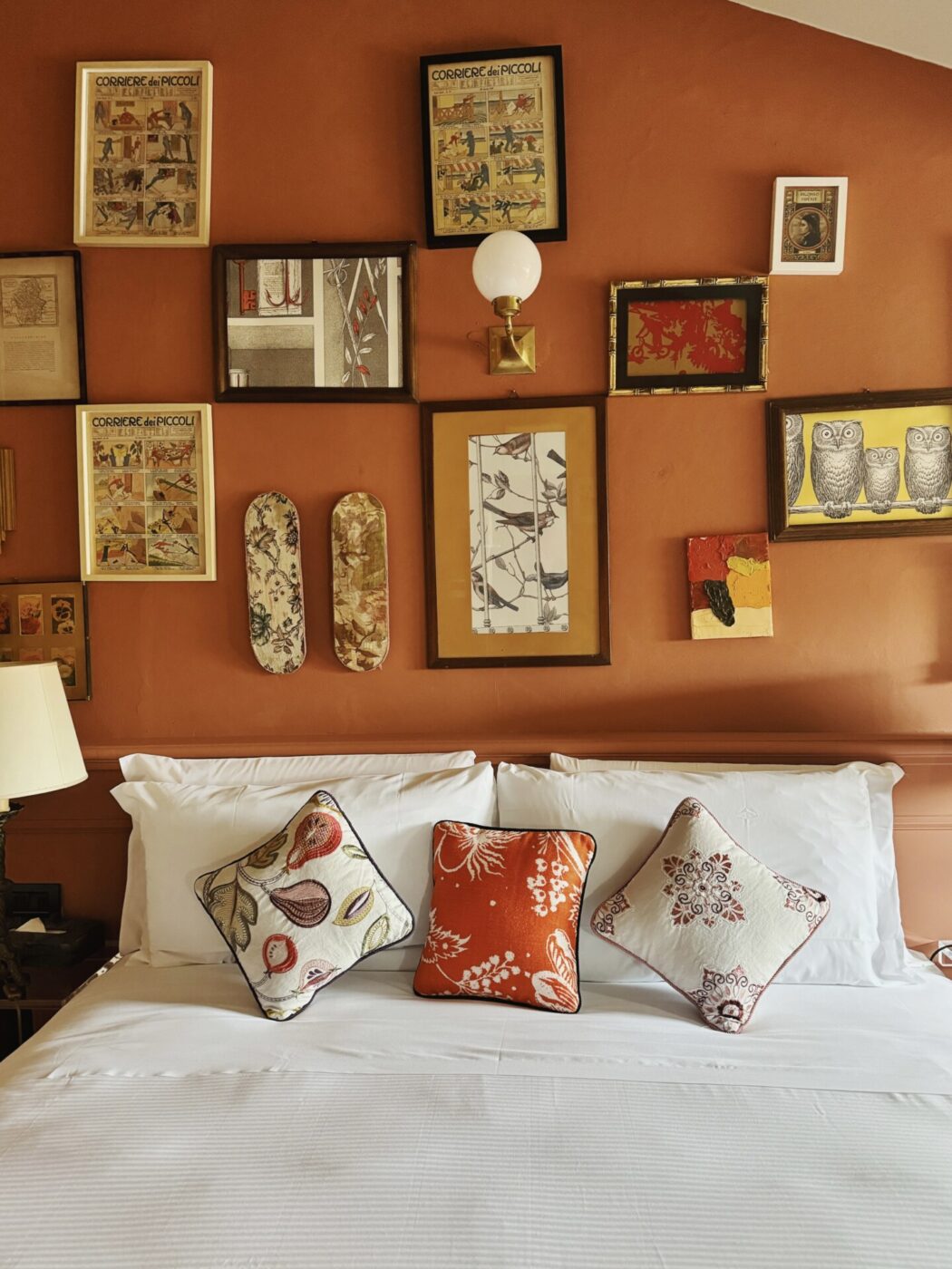 a room at stella d'italia with a white bed against an orange wall covered with framed images of patterns and prints