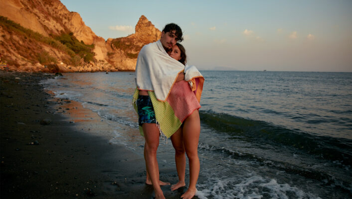 a still from the movie about Bagnoli showing a girl and a guy hugging under a beach towel by the sea