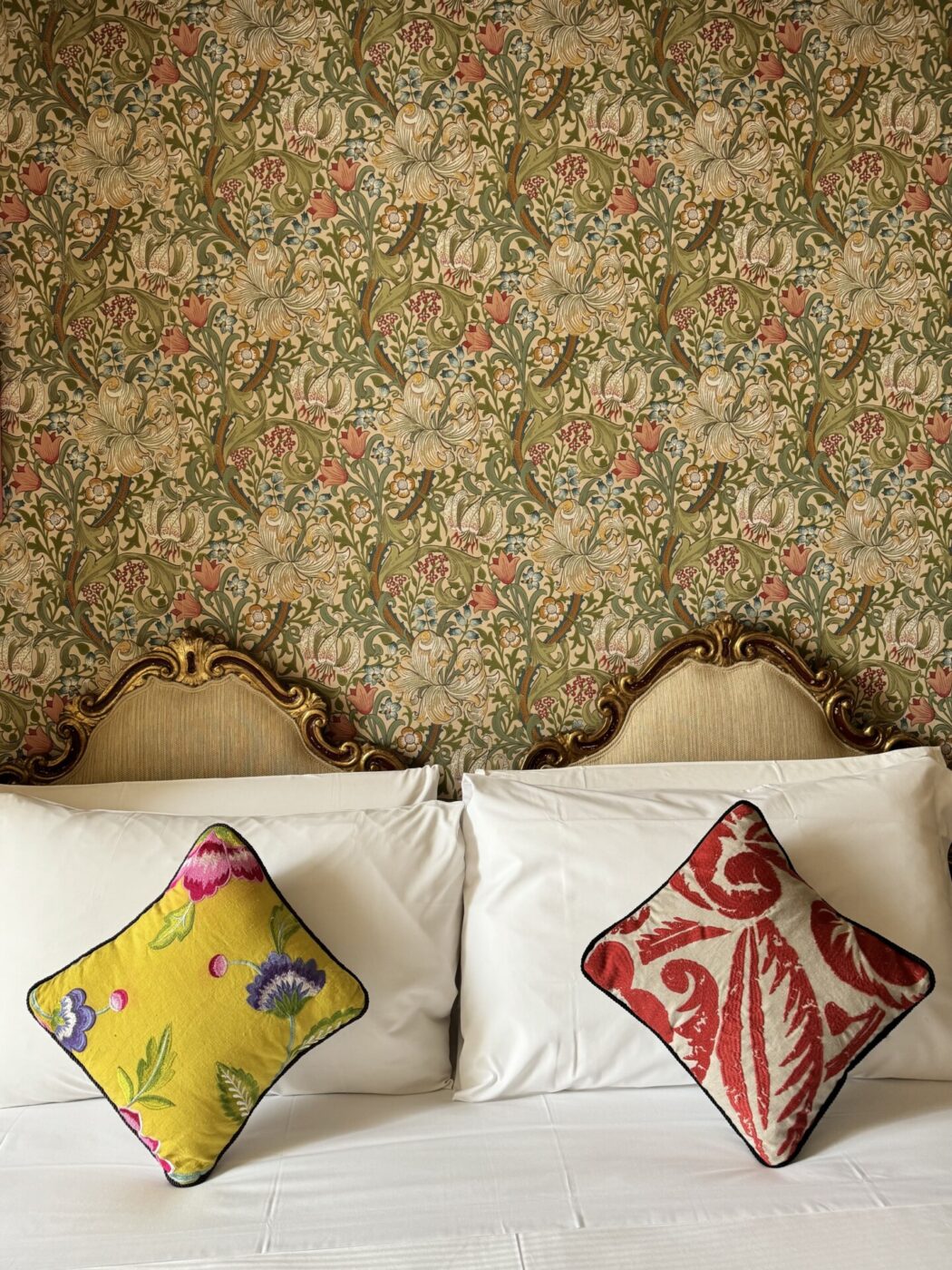 an image of the beds at stella d'italia with an ornate frame against a pretty wall papered wall and two mismatched colored pillows
