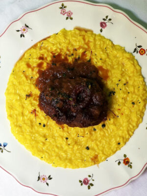 ossobucco on top of risotto alla milanese on a floral-patterned plate