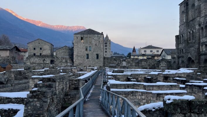 an image of some of the Roman ruins in Aosta covered in snow at sunset